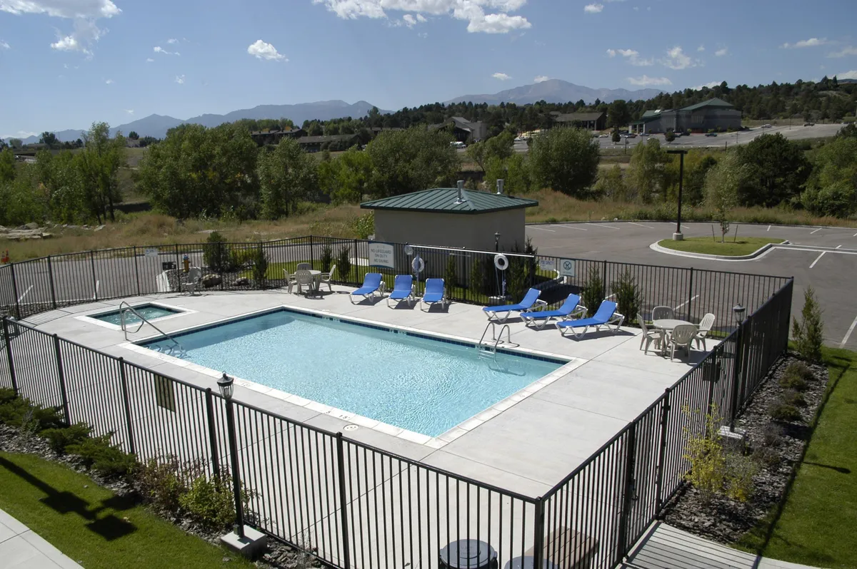 This exterior shot showcases the swimming pool from a different angle, emphasizing the sun loungers, landscaped greenery, and a poolside cabana. The setting suggests an atmosphere perfect for pool parties, afternoon reading, and sunbathing, reinforcing the idea of a resort-like experience close to nature.