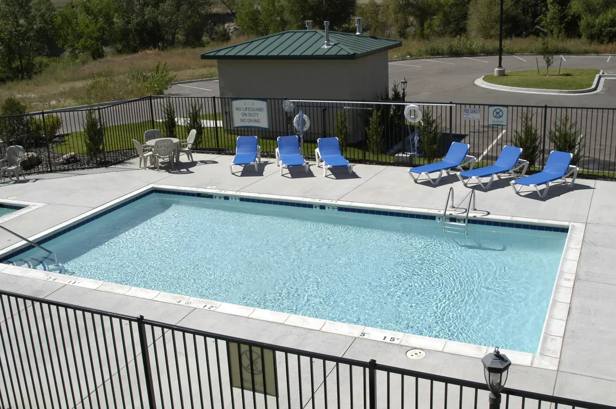 This image captures the inviting outdoor swimming pool surrounded by lounge chairs and a landscaped area, with safety signage visible. The scene is set during a leisurely time, possibly sunset, creating a relaxed atmosphere ideal for families unwinding after a day of adventure. The pool area evokes images of splash-filled evenings, socializing, and relaxation.