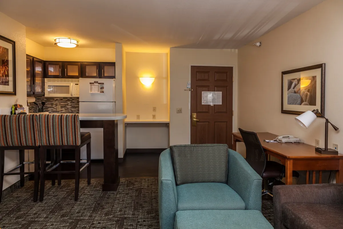 The image showcases the condo's inviting open-concept living space, featuring a modern kitchen with a breakfast bar, comfortable seating perfect for socializing or sharing meals, a dedicated desk area for remote work, and a welcoming entryway.